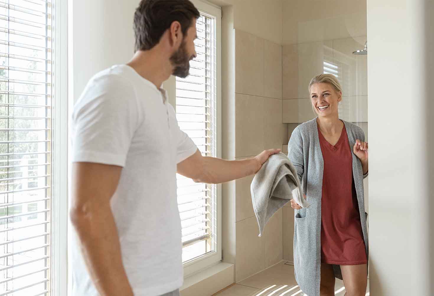 Ein Mann reicht einer Frau ein Handtuch im Badezimmer