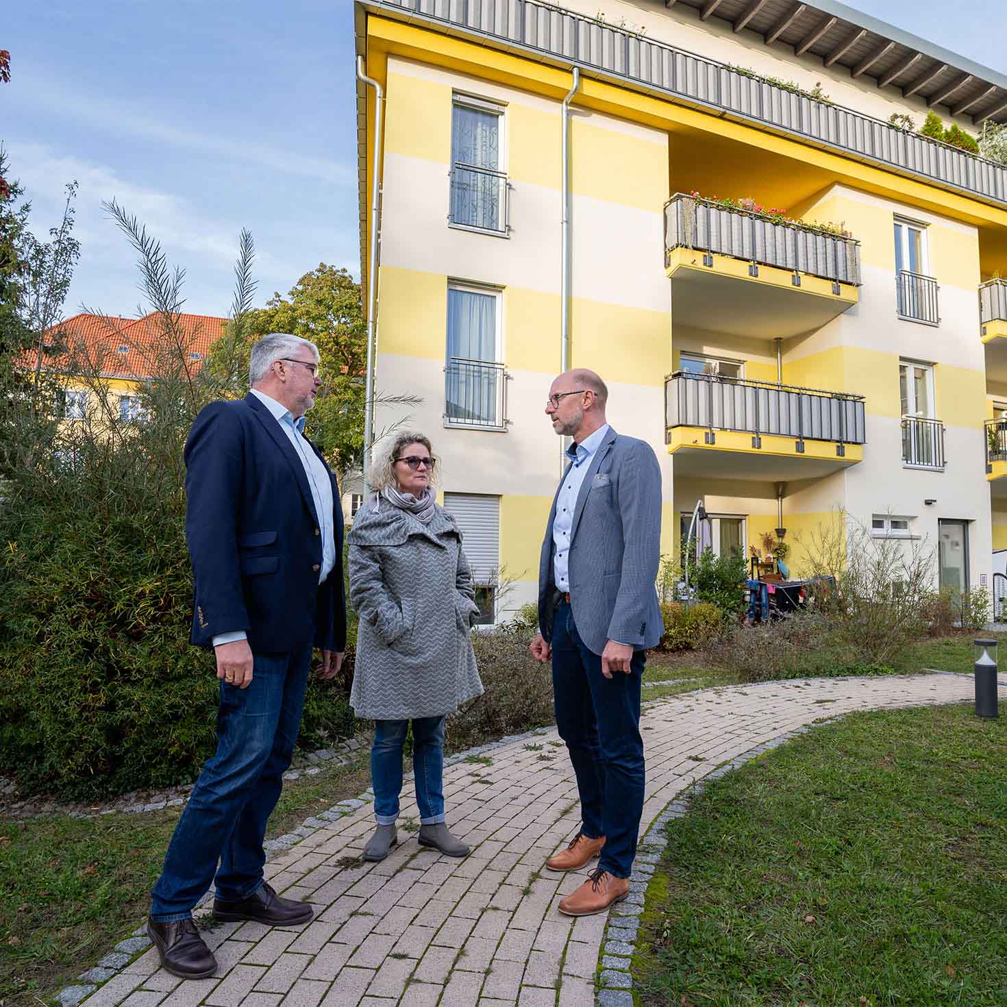 Drei Personen unterhalten sich vor einer Wohnanlage