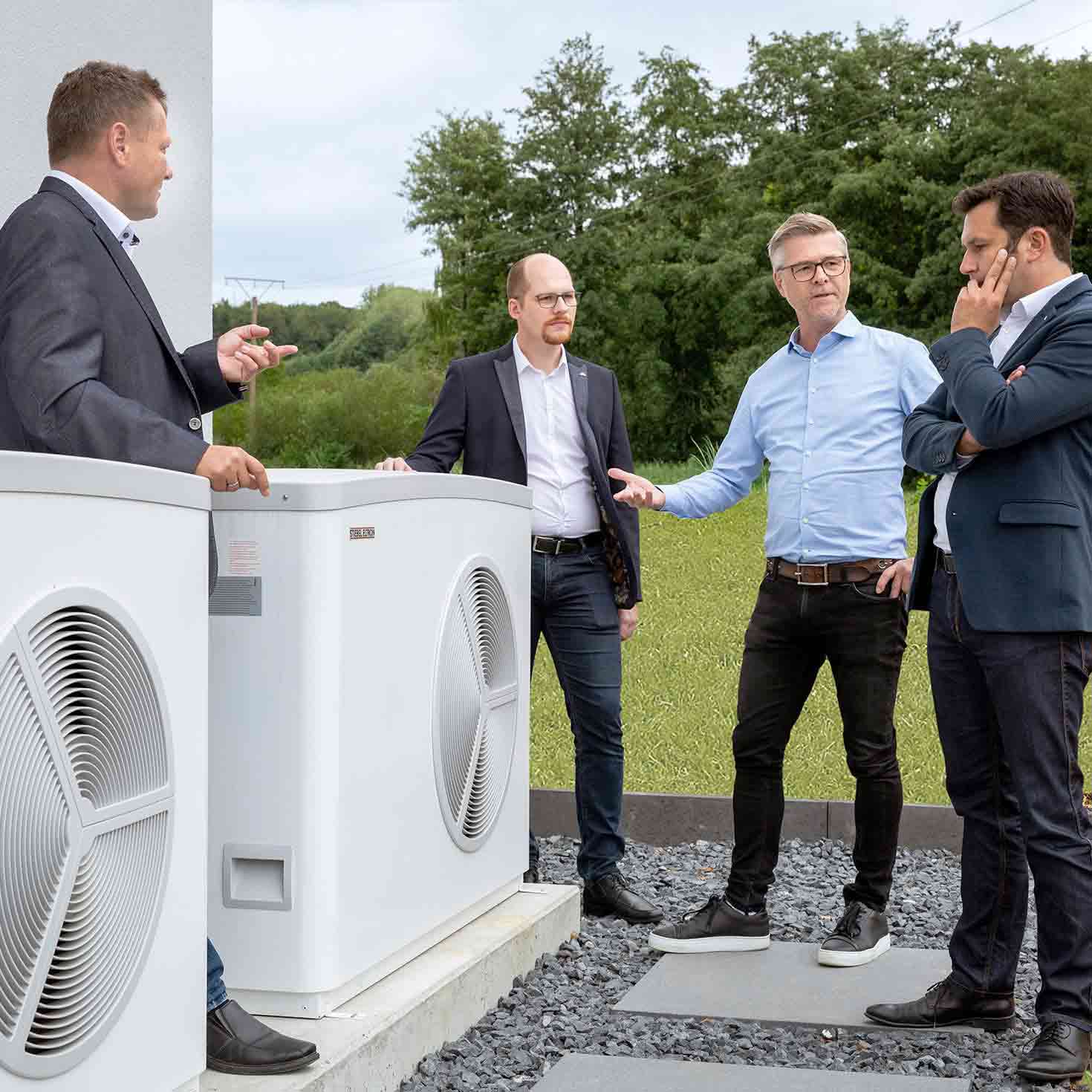 Eine Gruppe von Männern steht um eine Wärmepumpe und unterhält sich