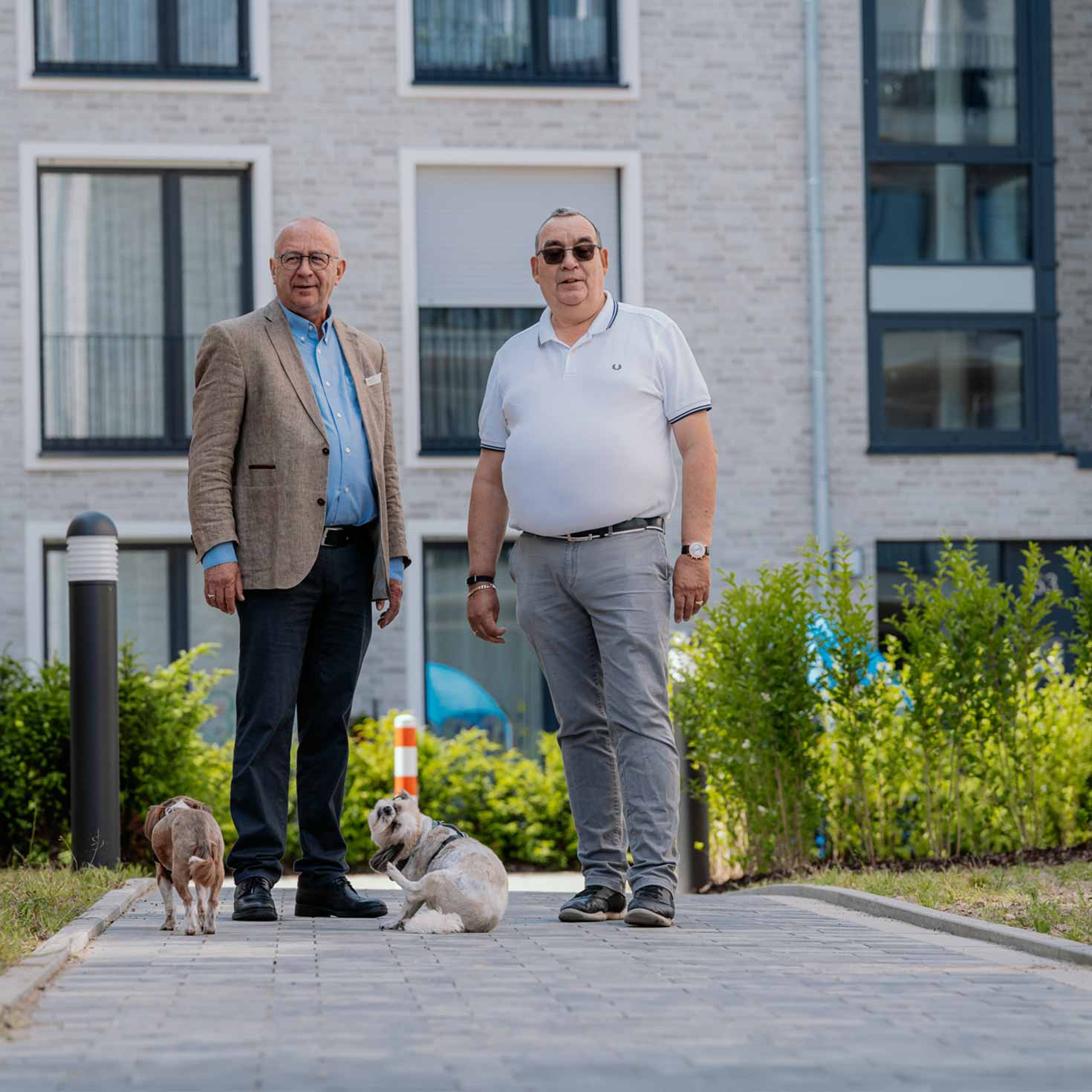Die Bauherren stehen mit ihren Hunden auf einem gepflasterten Fußweg