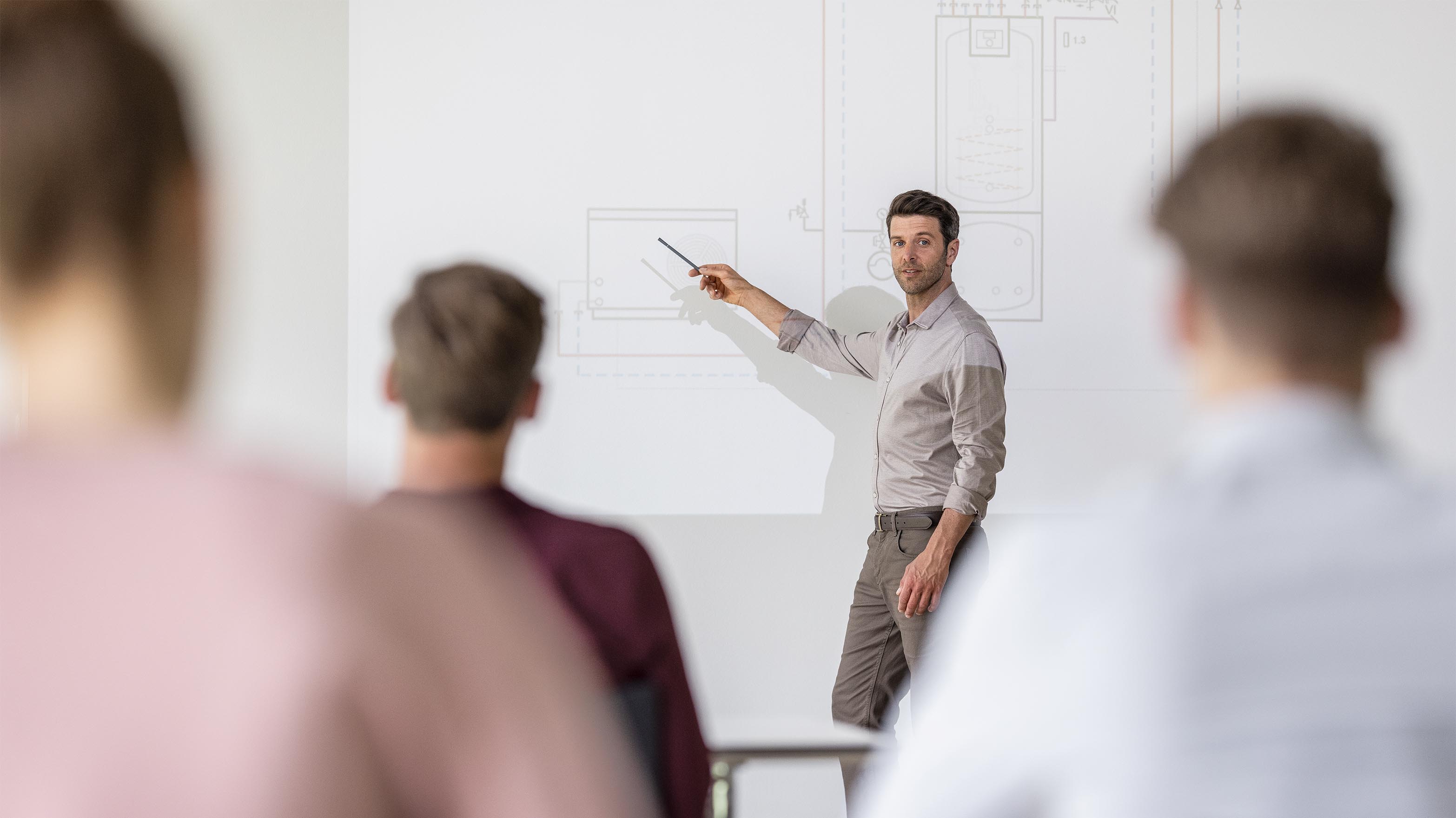 Schulungsreferent steht am Board und erklärt STIEBEL ELTRON-Wärmepumpen. Auf dem Screen ist eine technische Zeichnung zu sehen.