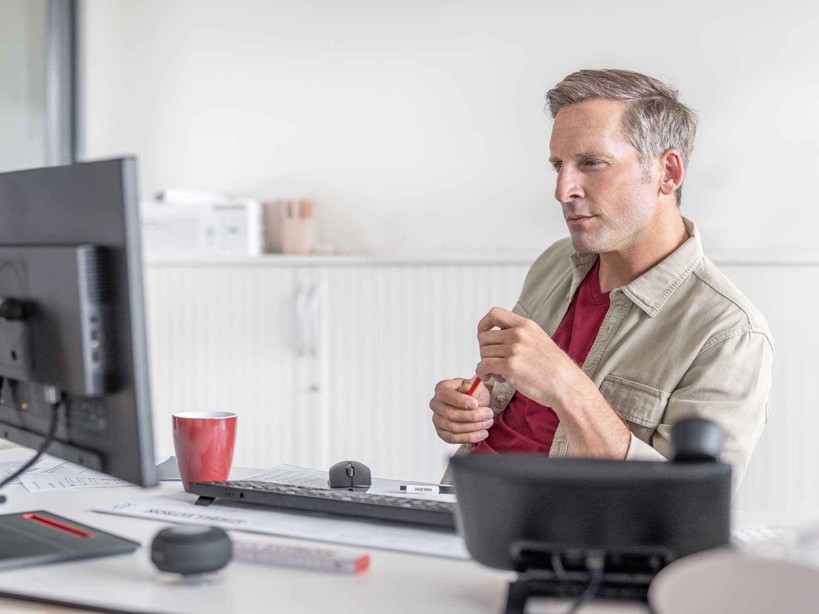 Mann sitzt am Schreibtisch und betrachtet den Desktop