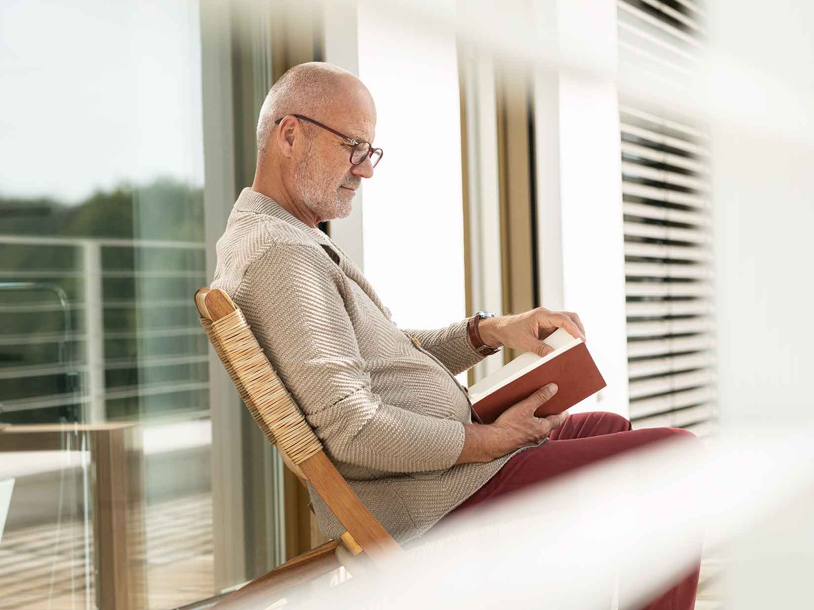 Ein Mann sitzt auf seiner Terrasse und blättert in einem Buch