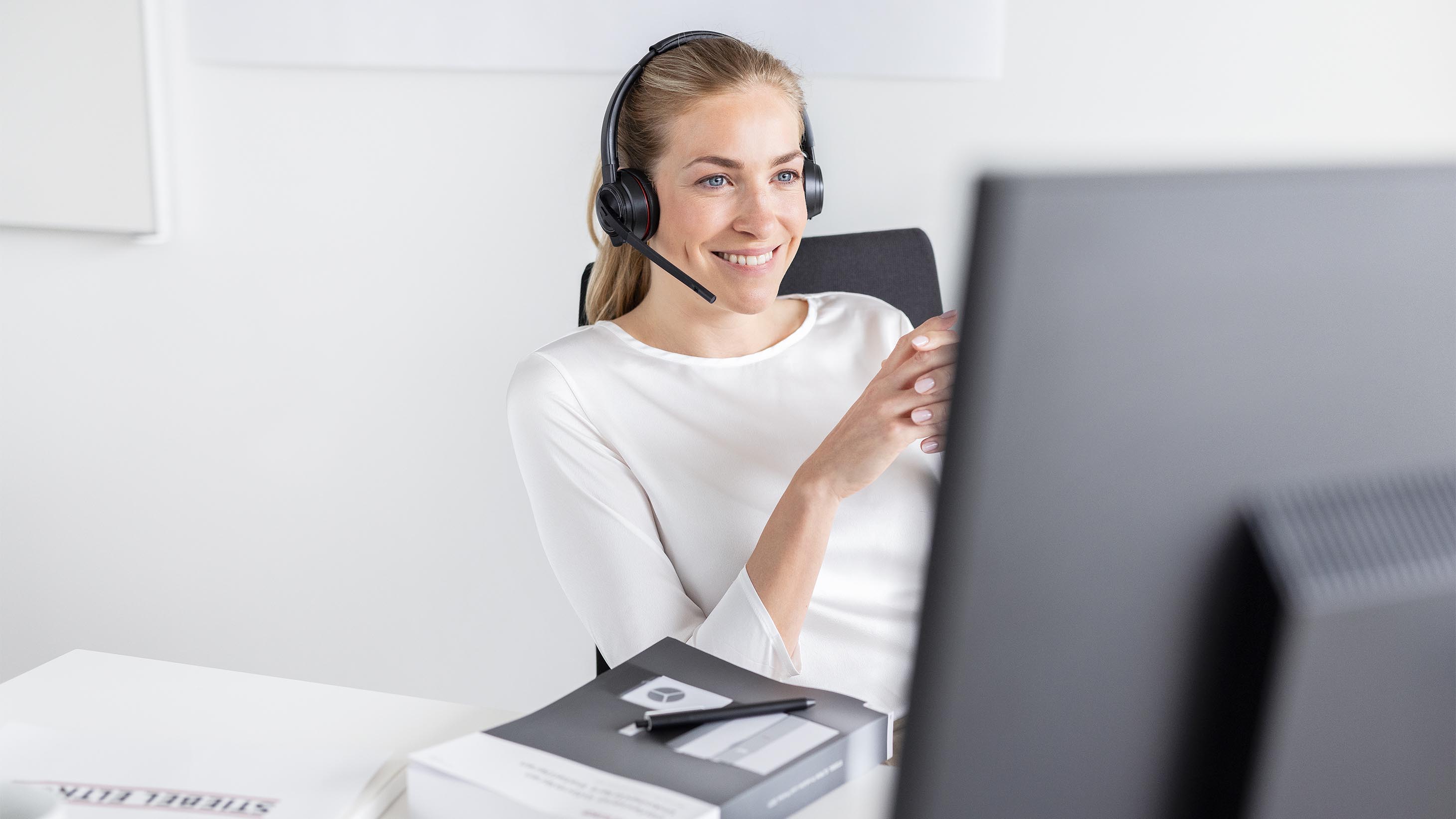 Frau sitzt mit Headset vor dem Monitor