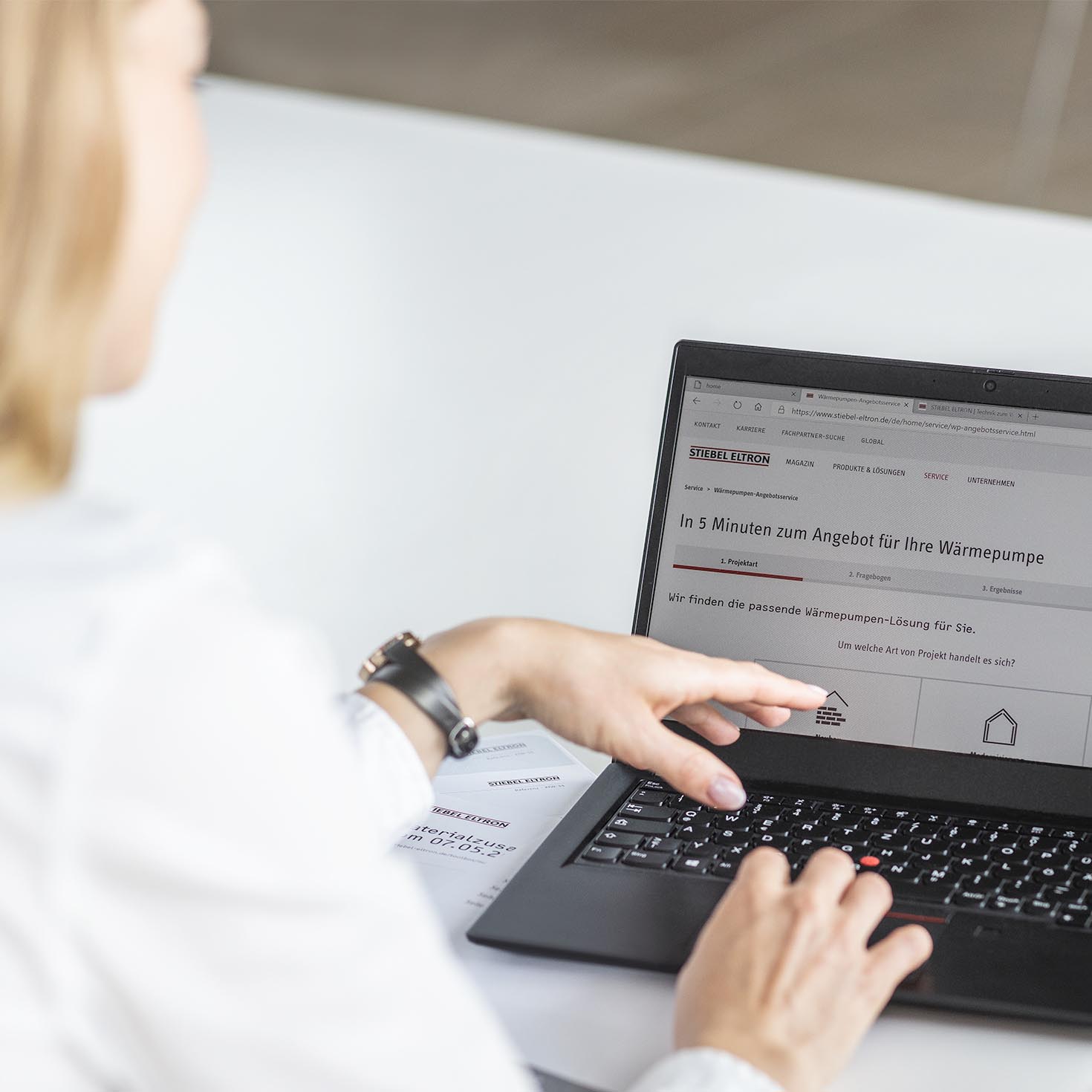 Frau bedient an ihrem Laptop den Wärmepumpenangebotsservice, auf dem Bildschirm ist die Startseite des STIEBEL ELTRON Services zu sehen