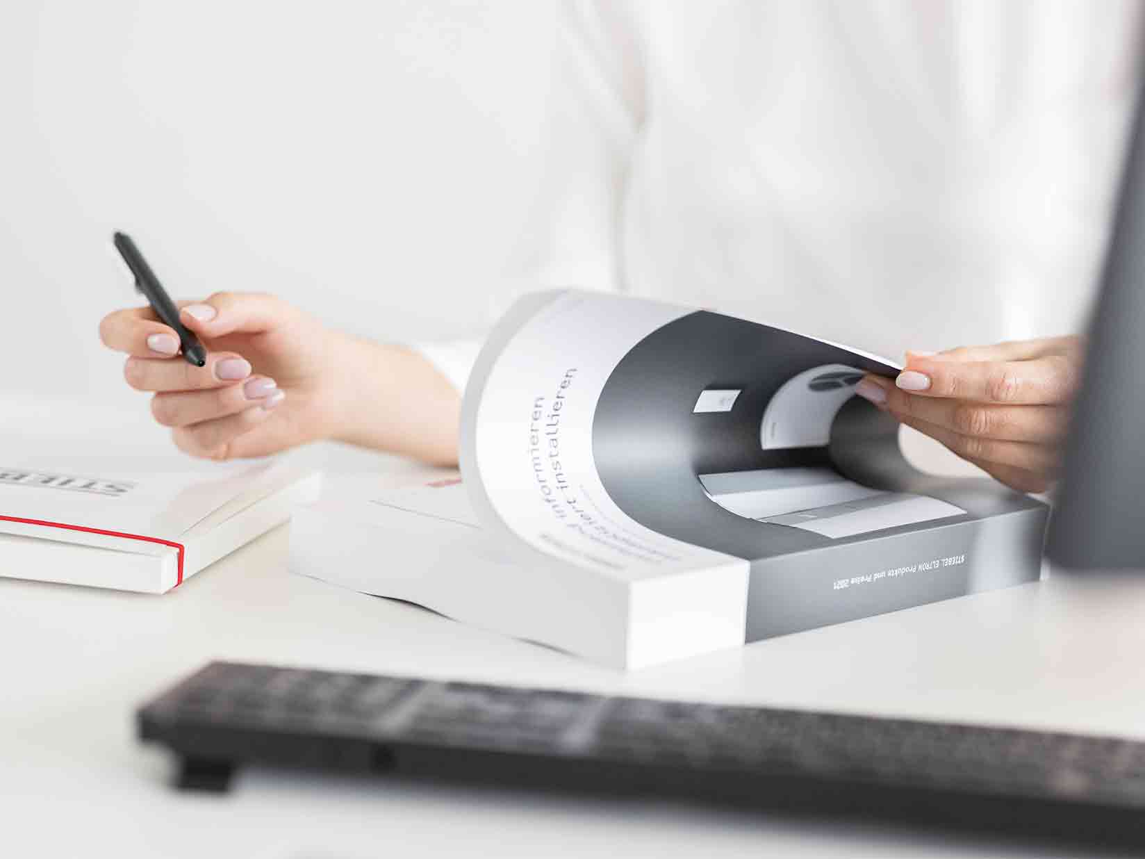 Eine Frau blättert im STIEBEL ELTRON Systemhandbuch. In der rechten Hand hält sie einen Stift