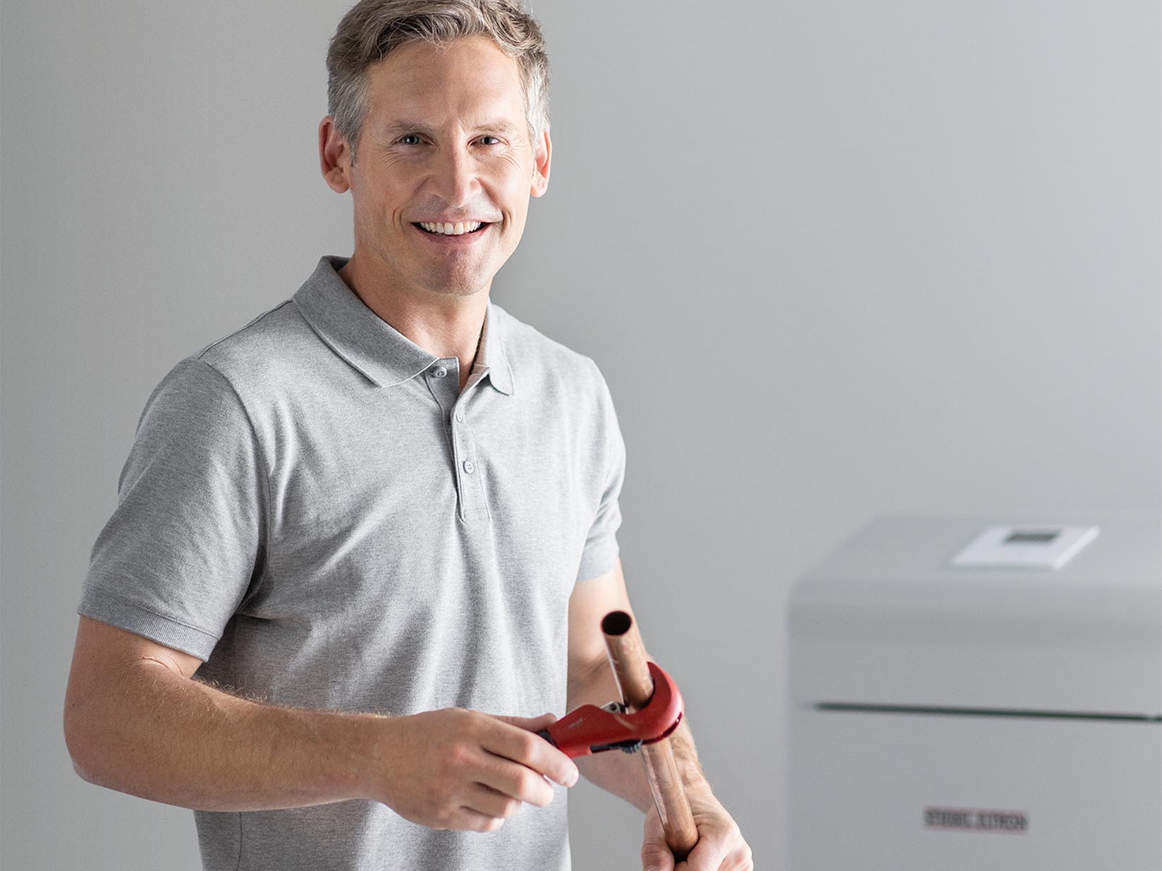 Fachhandwerker steht mit Rohr und Rohrzange in der Hand vor einer STIEBEL ELTRON Wärmepumpe