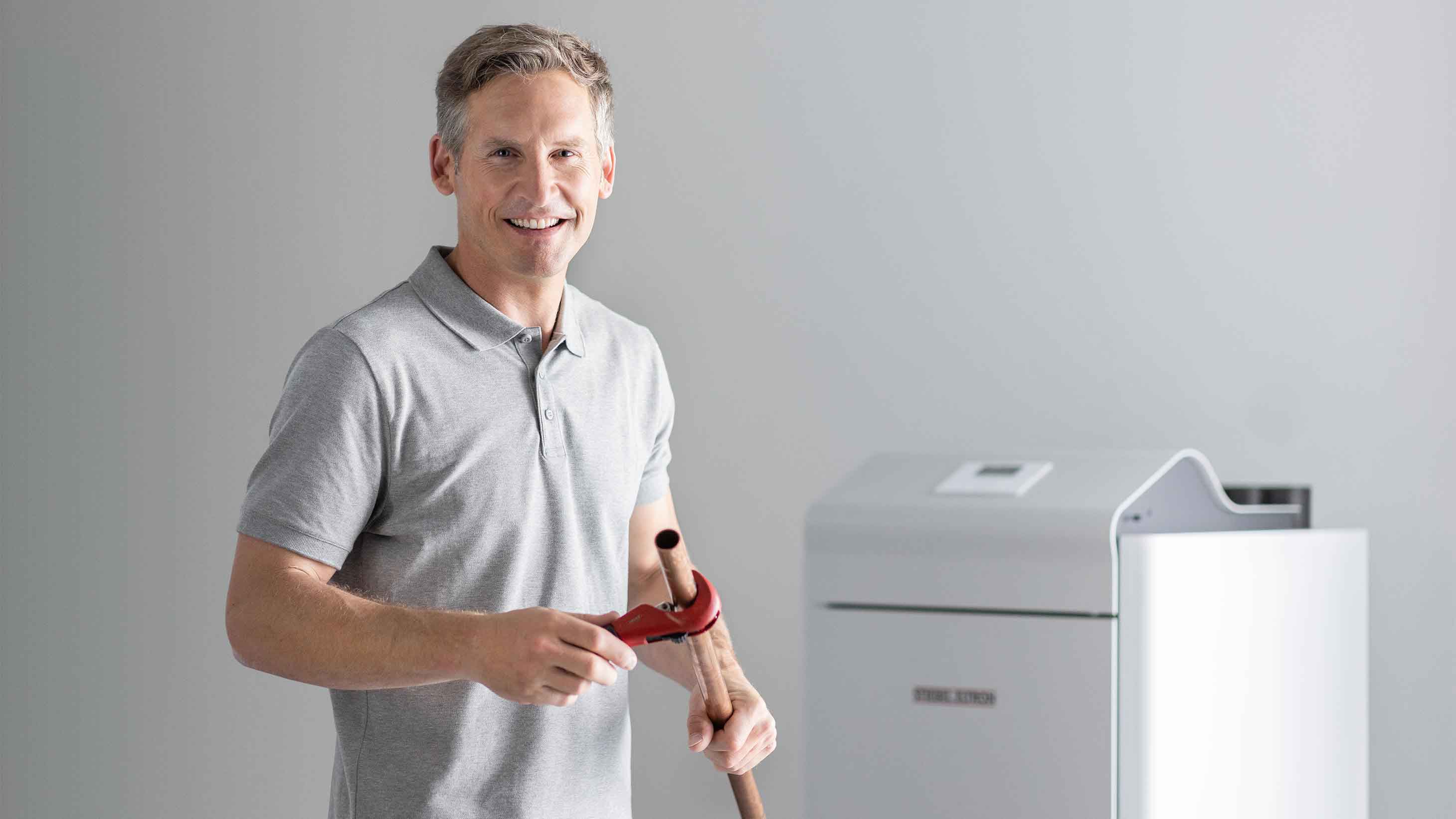 Fachhandwerker hält Rohr und Rohrzange in der Hand und steht vor einer STIEBEL ELTRON-Wärmepumpe