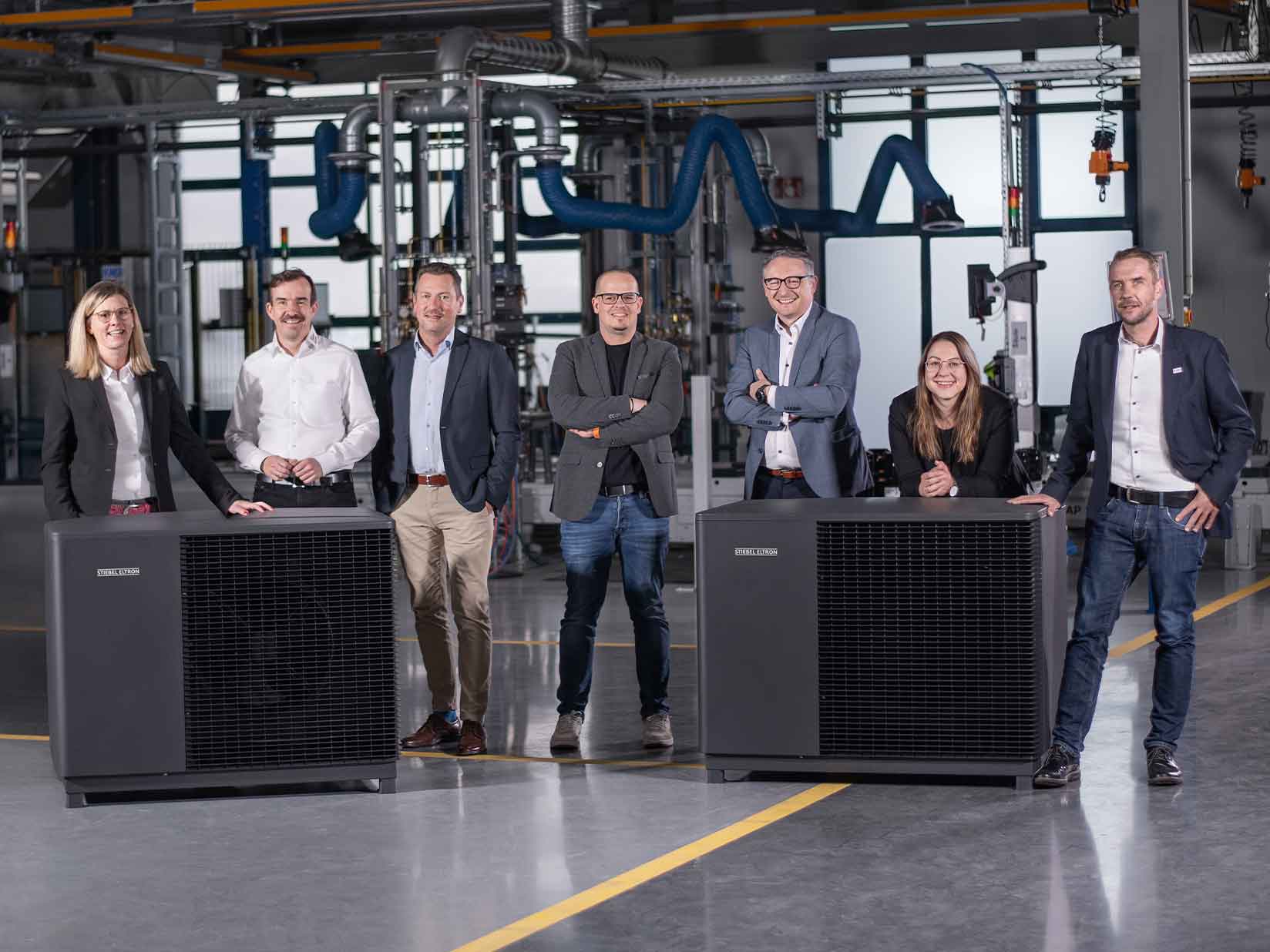STIEBEL ELTRON-Mitarbeiter stehen neben einer Luftwärmepumpe in einer Fertigungshalle