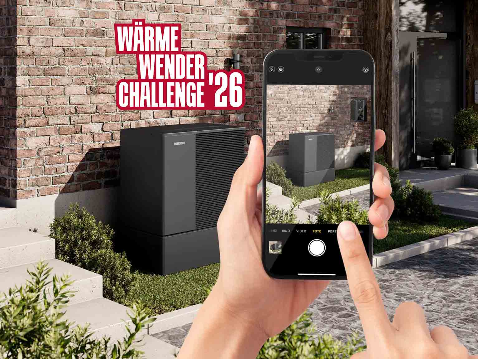 Ein Handy fotografiert eine Wärmepumpe vor roter Backsteinhauswand, oben links ist das Logo Wärmewender Challenge 26 eingeblendet