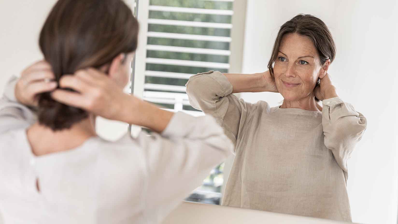 Eine Frau steht in einem Bad vor dem Spiegel und richtet sich die Haare