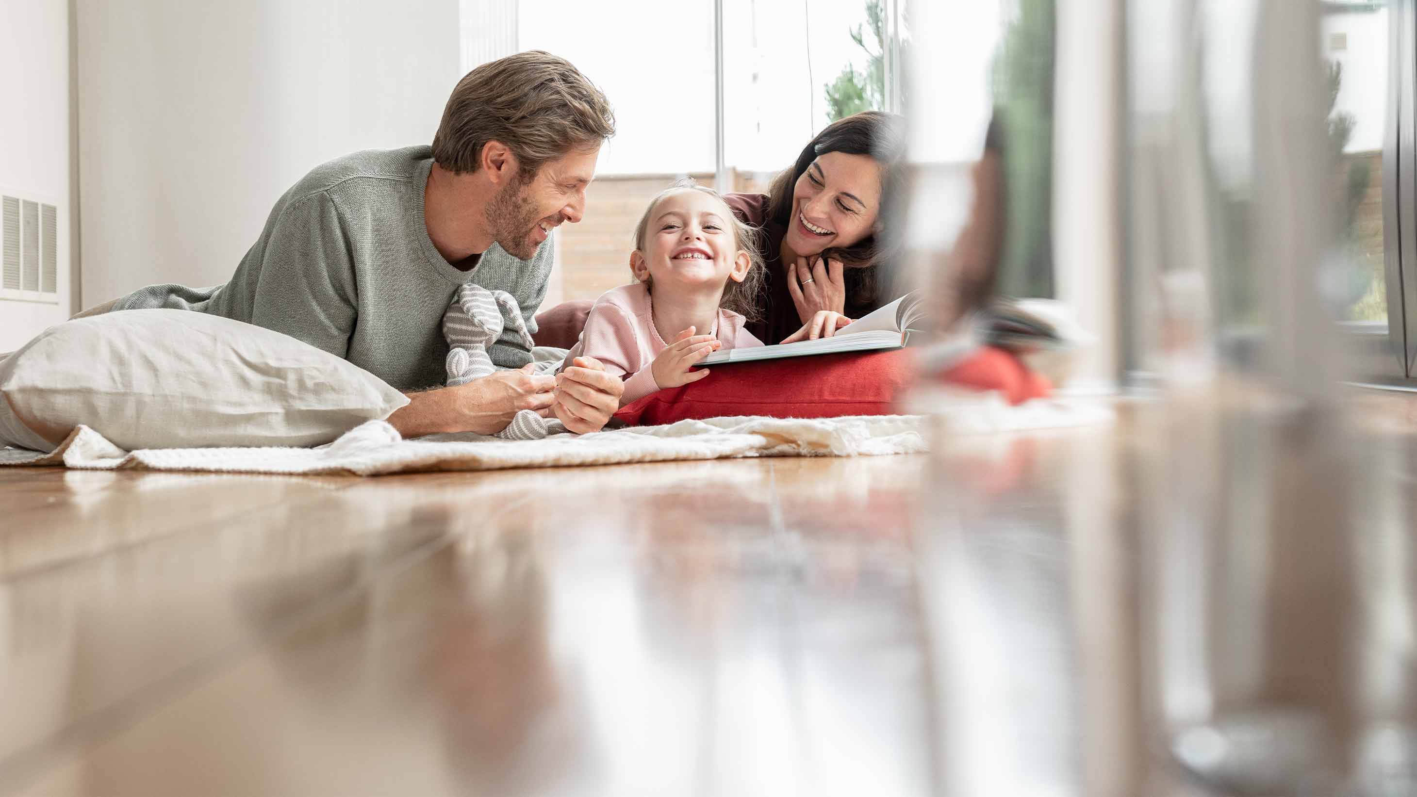 Eine Familie liegt auf dem Boden und schaut in ein Buch.