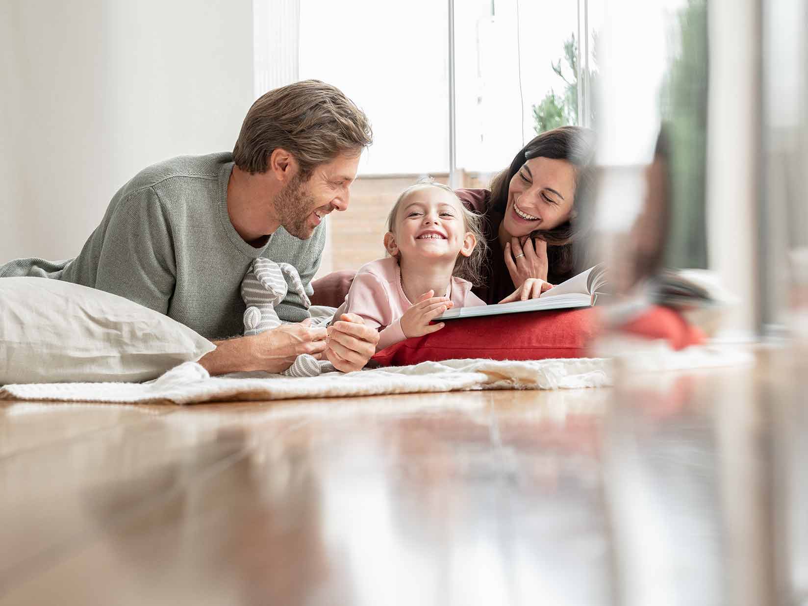 Eltern liegen mit ihrer Tochter auf dem Fußboden und lesen ein Buch.