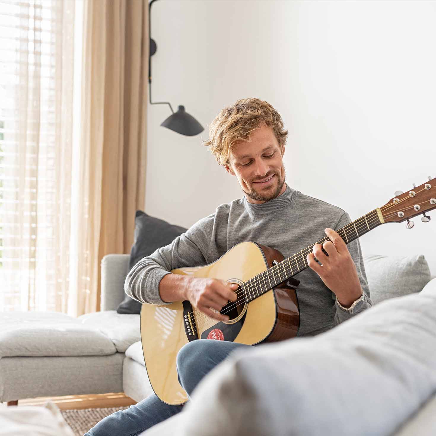 Mann spielt im Wohnzimmer auf seiner Gitarre.