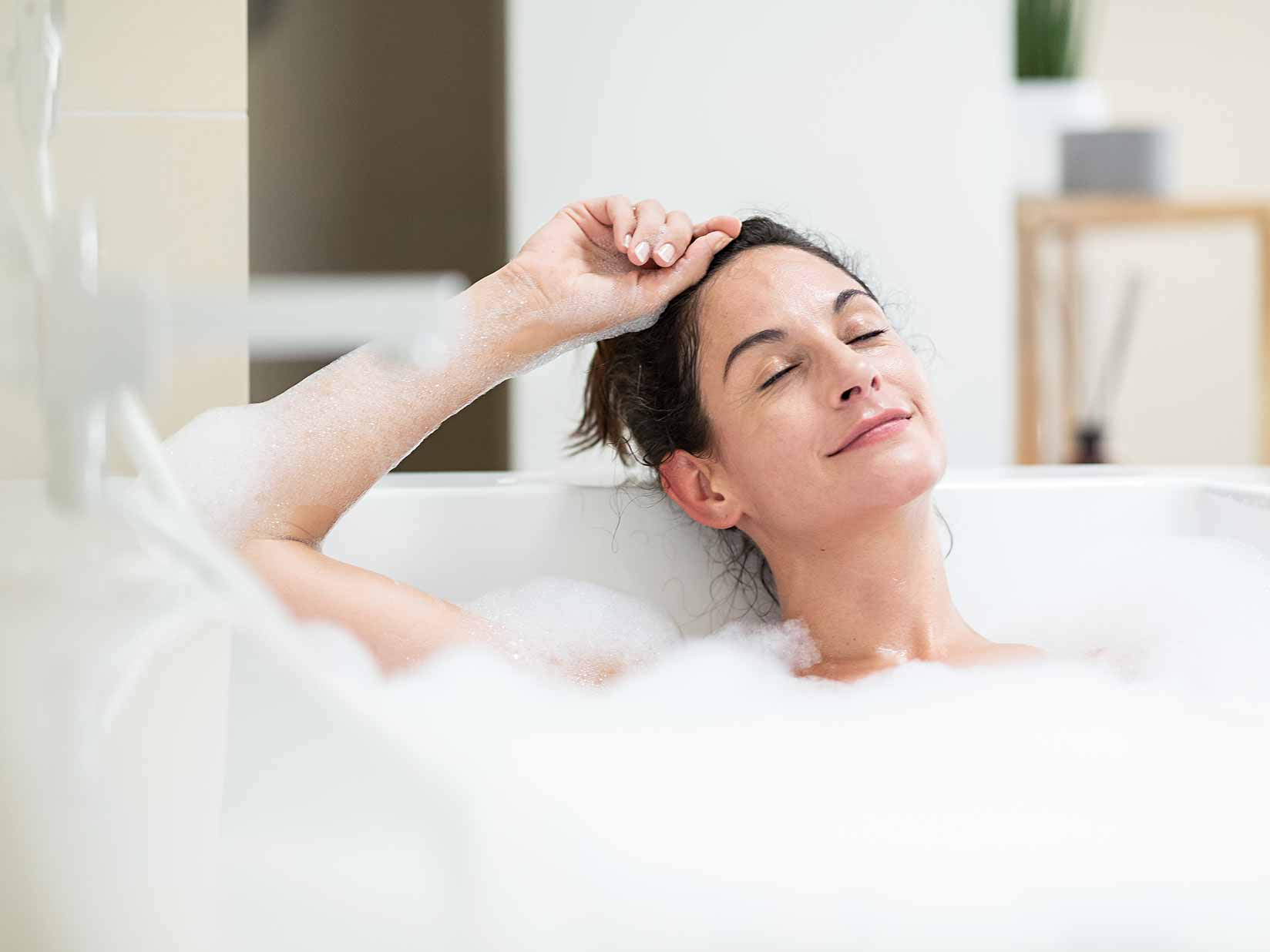 Frau liegt in der Badewanne und hat die Augen geschlossen.