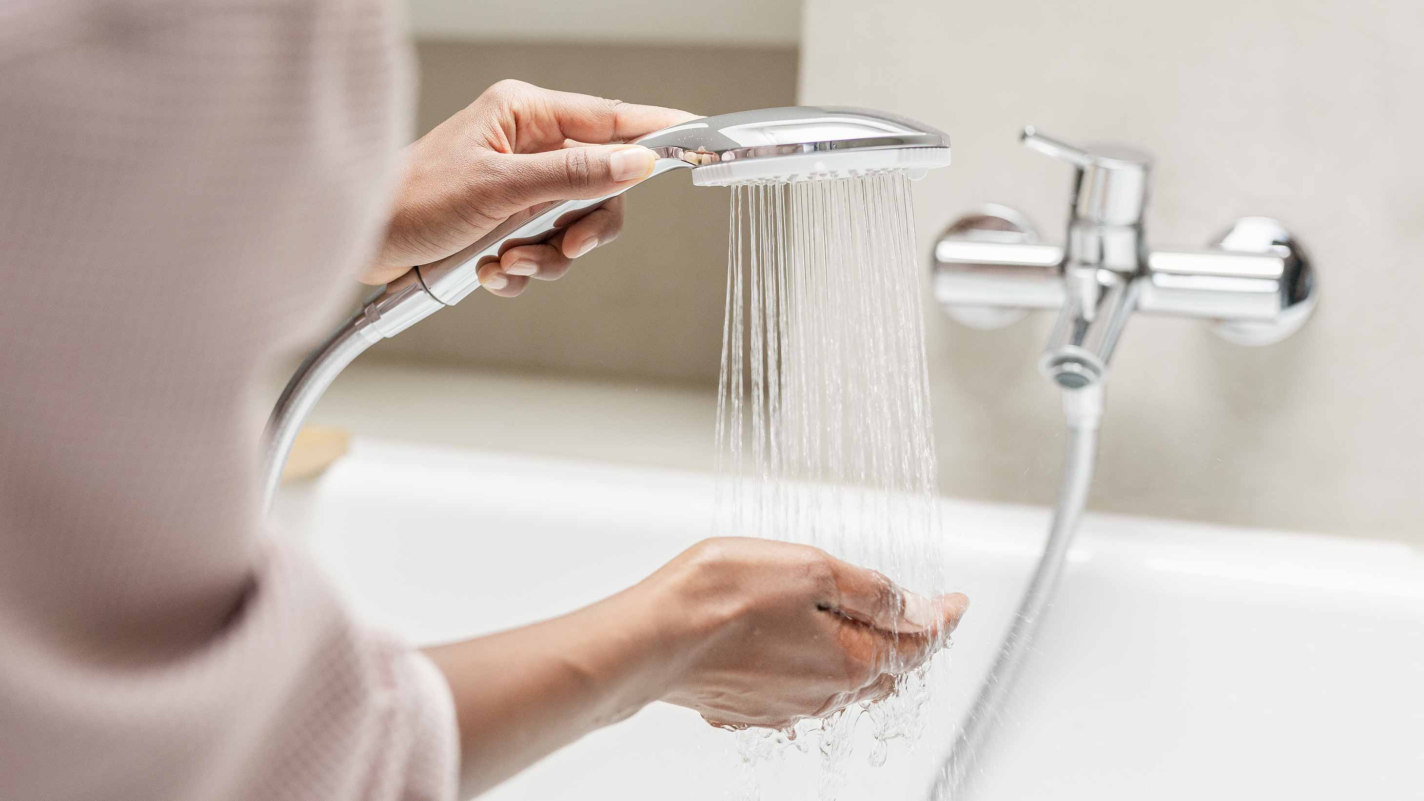 Frau hält eine laufende Duschbrause über der Badewanne