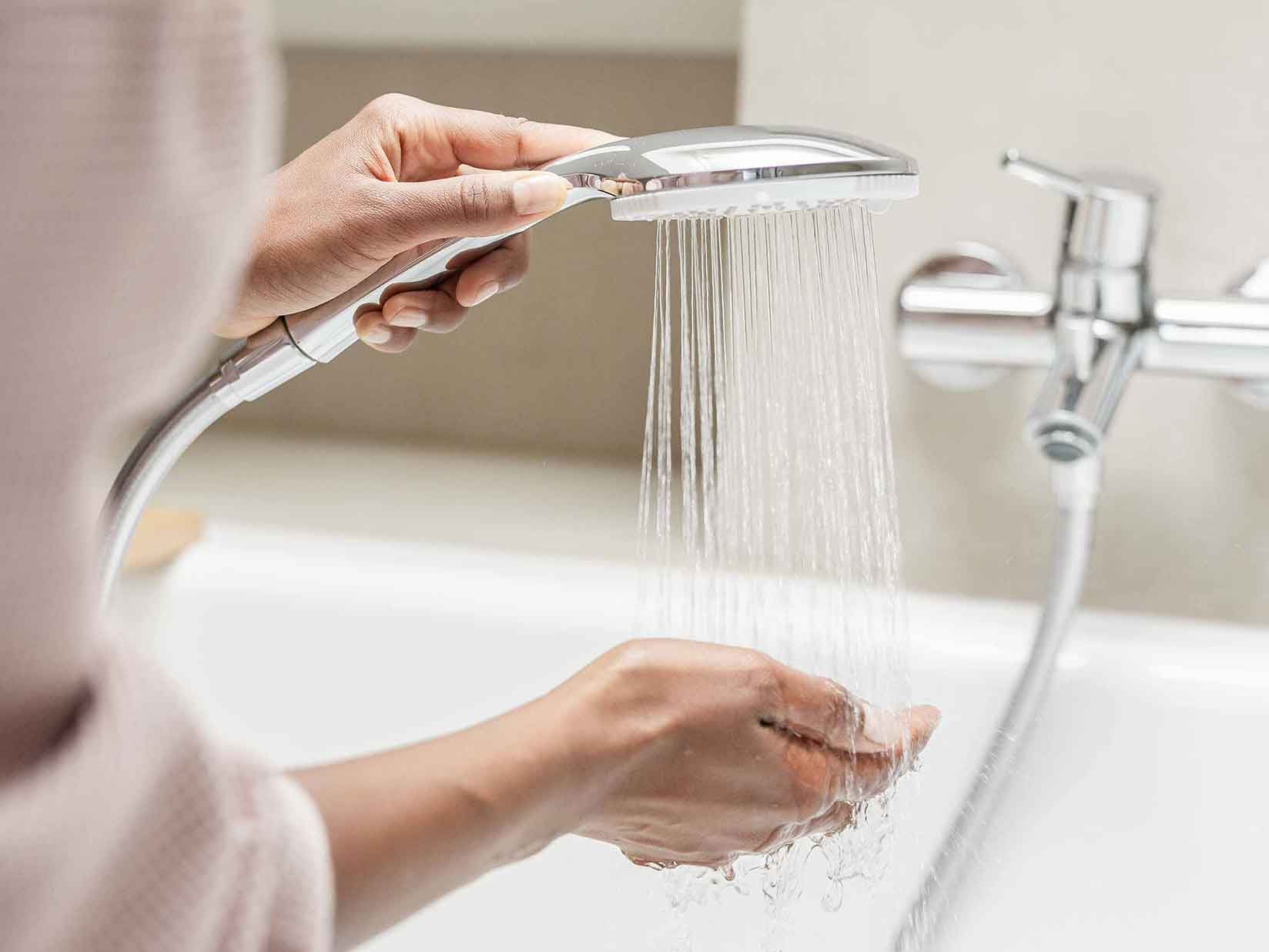 Eine Frau lässt warmes Wasser aus einer Duschbrause über Ihre Hand laufen.