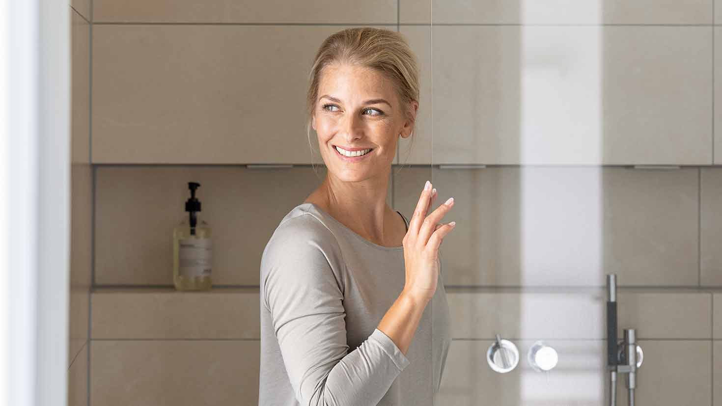 Eine blonde Frau lehnt an einer Glas-Duschtür