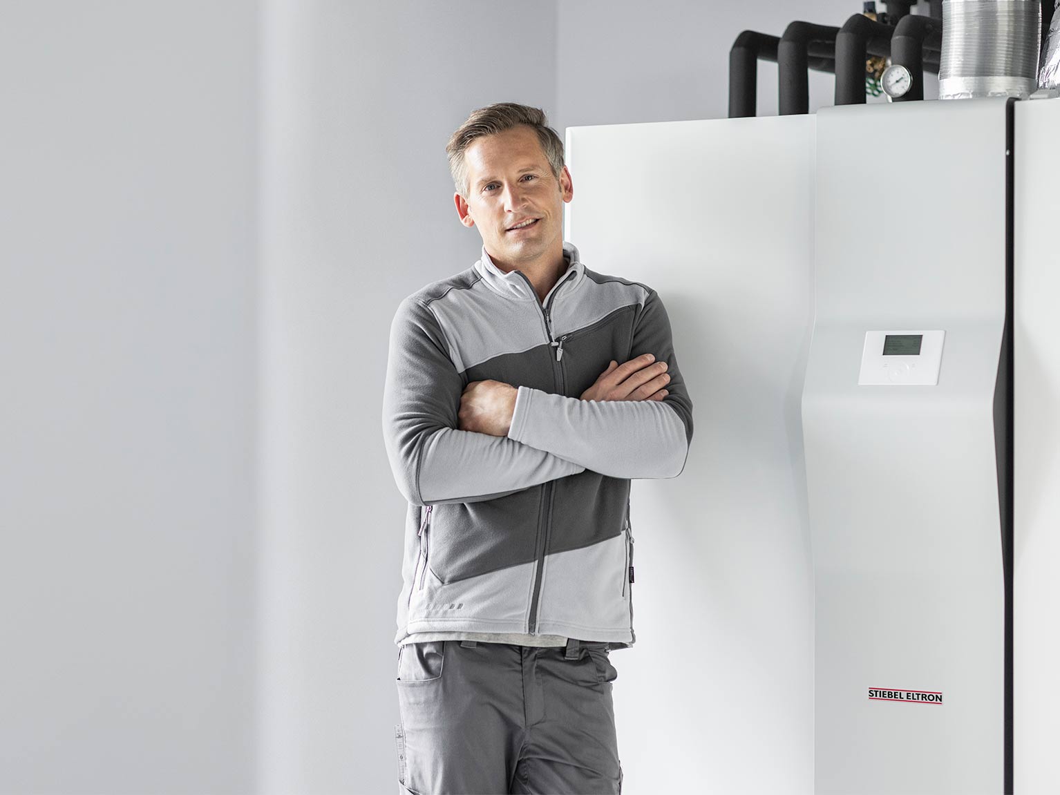 Fachhandwerker lehnt mit verschränkten Armen vor einem STIEBEL ELTRON-Integralgerät