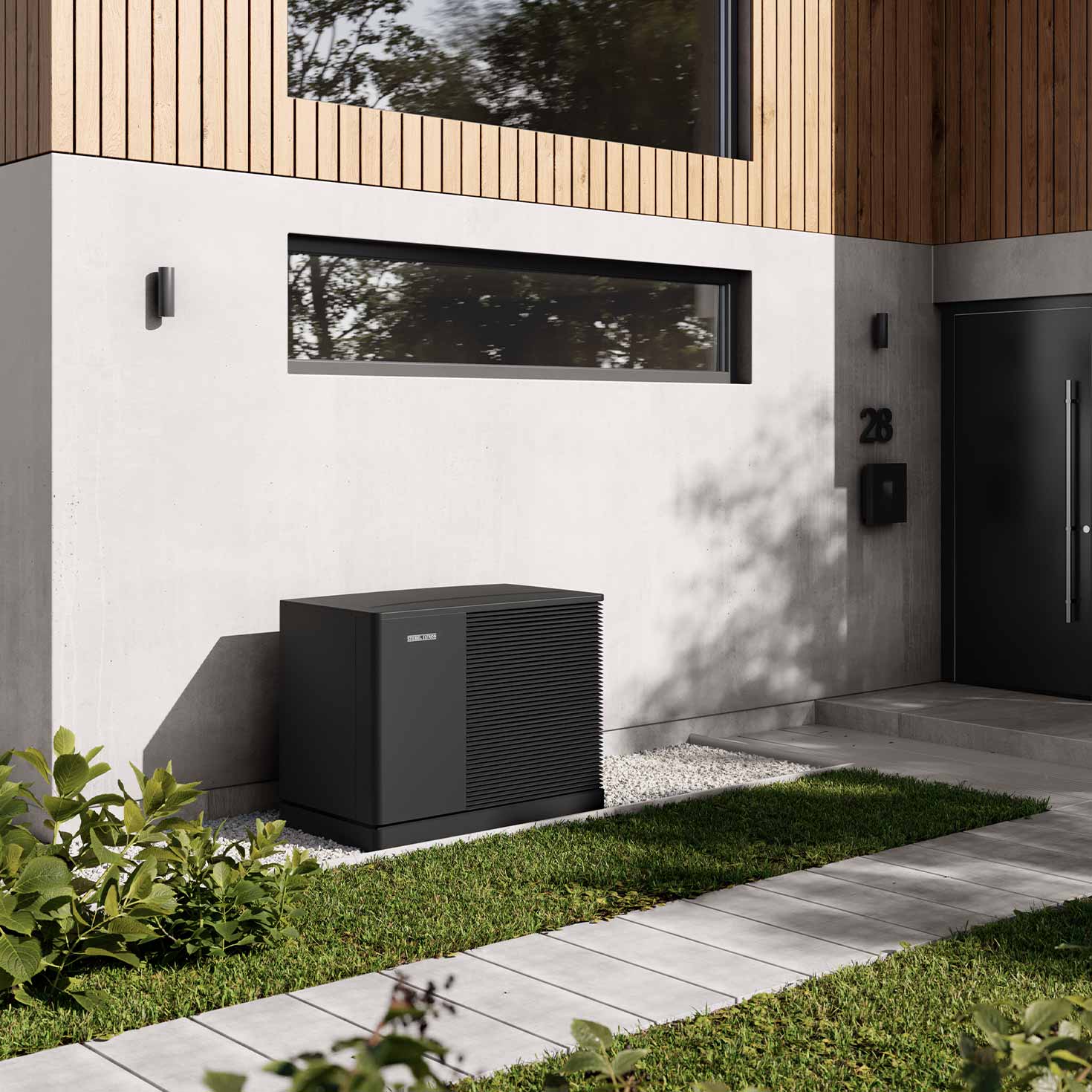 Eine schwarze Wärmepumpe steht vor der Fassade eines modernen Hauses auf einer Kiesfläche