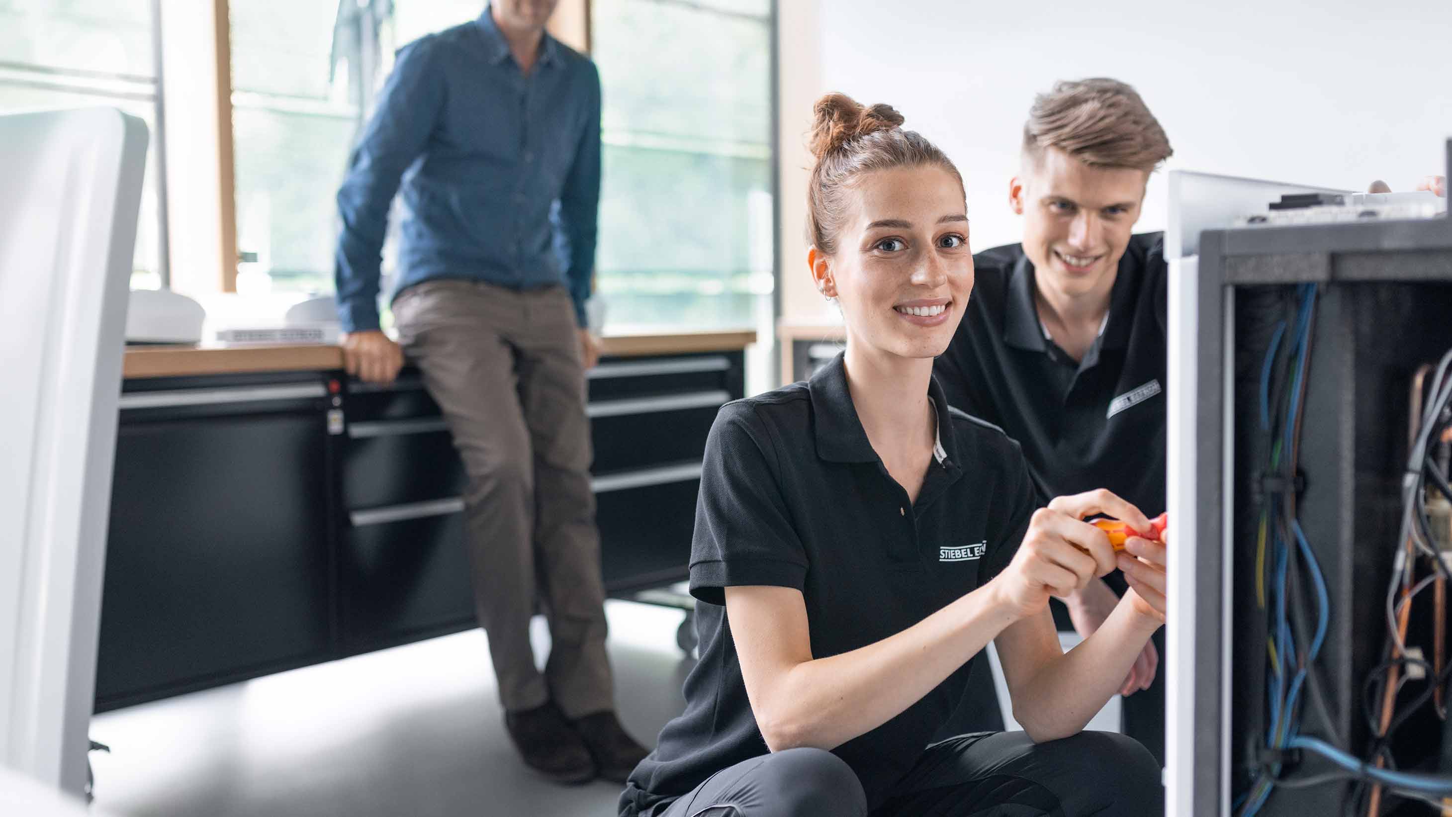 Zwei Auszubildende und ein Ausbilder vor einer Wärmepumpe von STIEBEL ELTRON