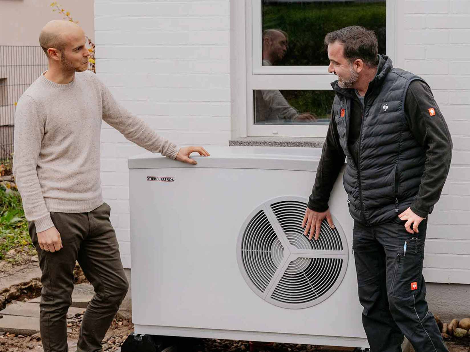 Zwei Männer stehen an einer Wärmepumpe und unterhalten sich