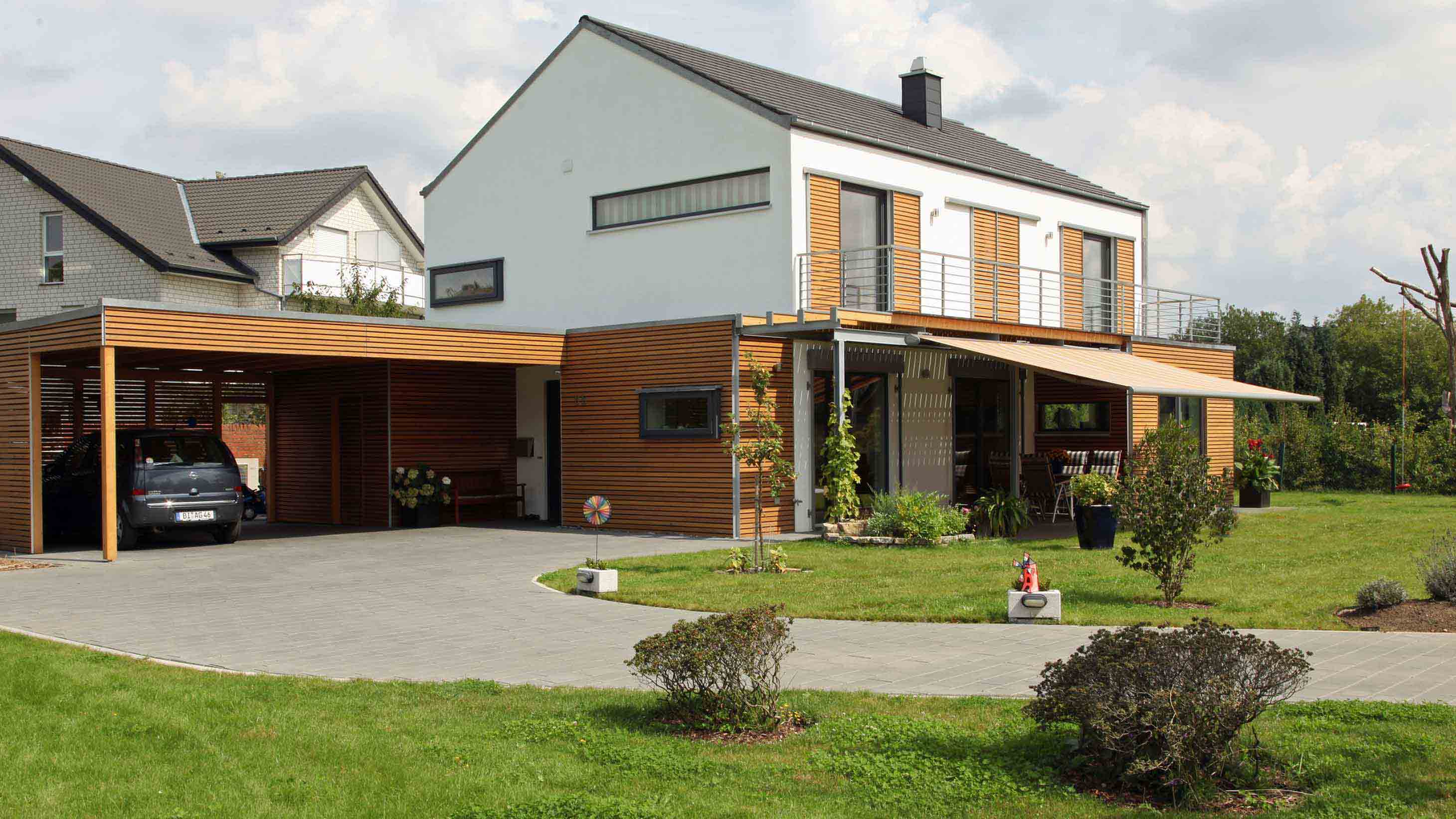 Ein modernes Einfamilienhaus mit Holzverkleidungen und einer gepflasterten Einfahrt mit Carport