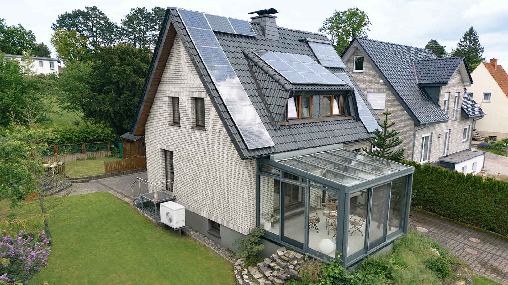Wärmepumpe steht vor Altbau mit Photovoltaik