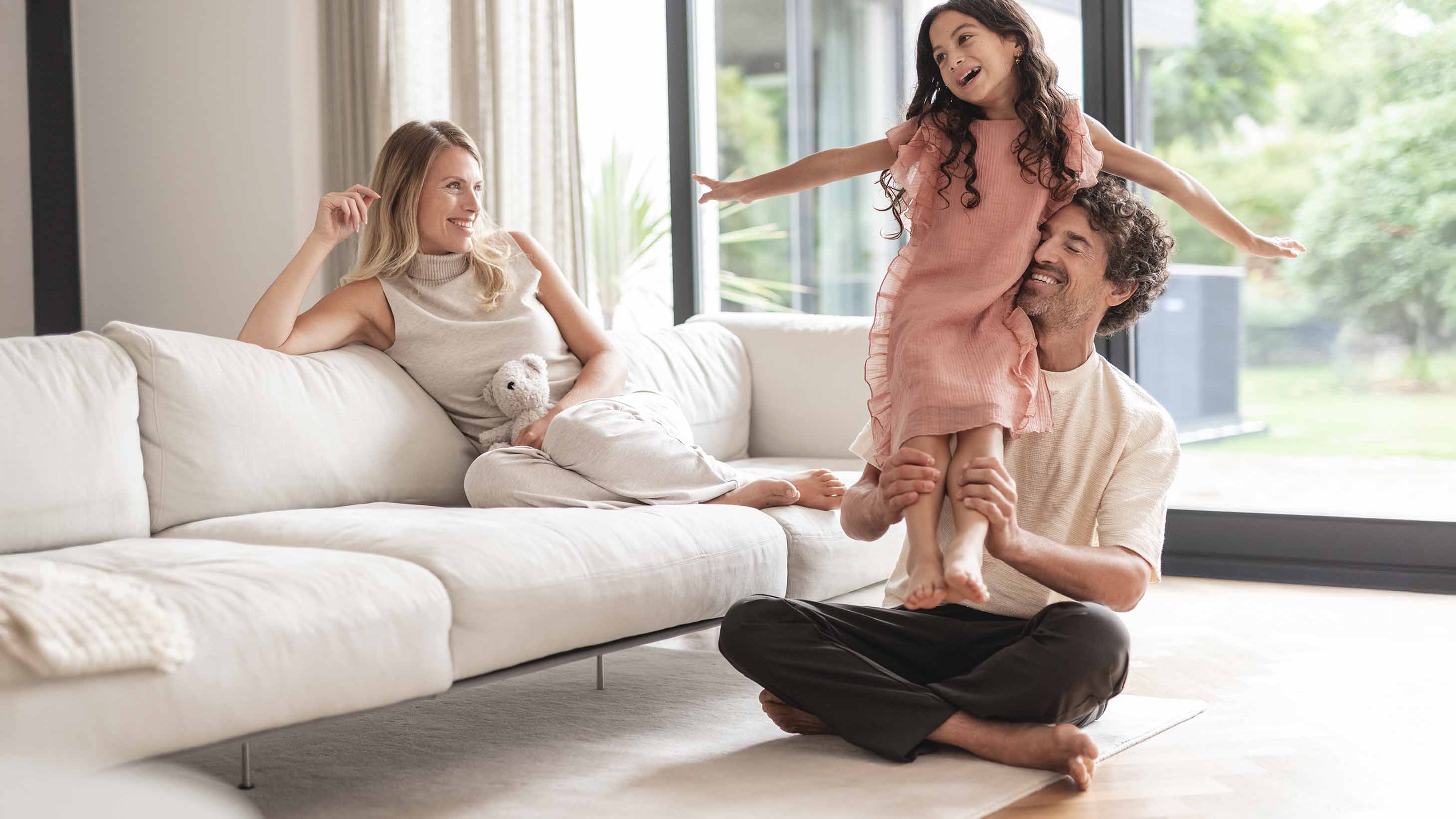Eine Familie spielt im Wohnzimmer. Im Hintergrund steht eine Wärmepumpe.