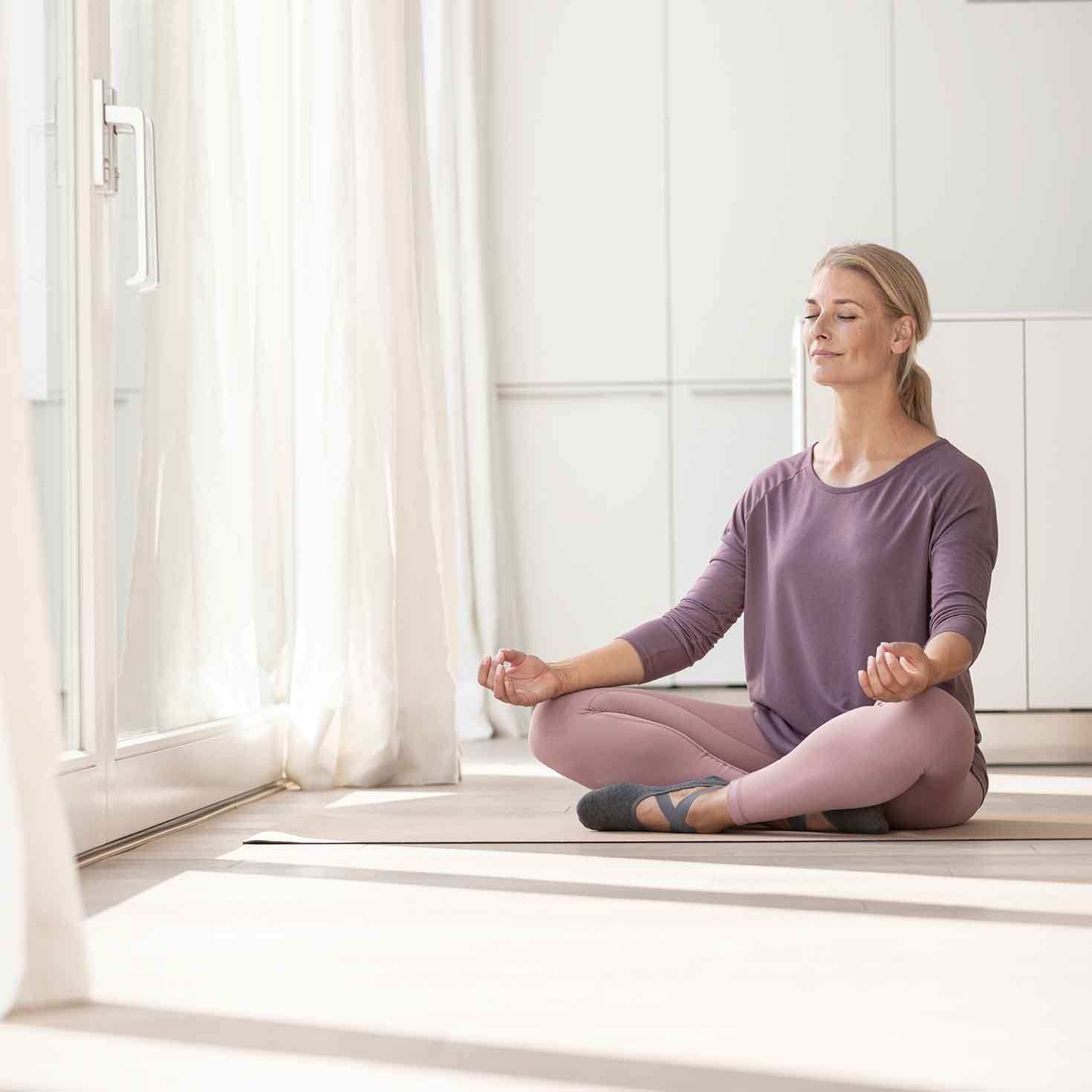 Frau sitzt im Schneidersitz auf dem Fußboden und macht Yoga