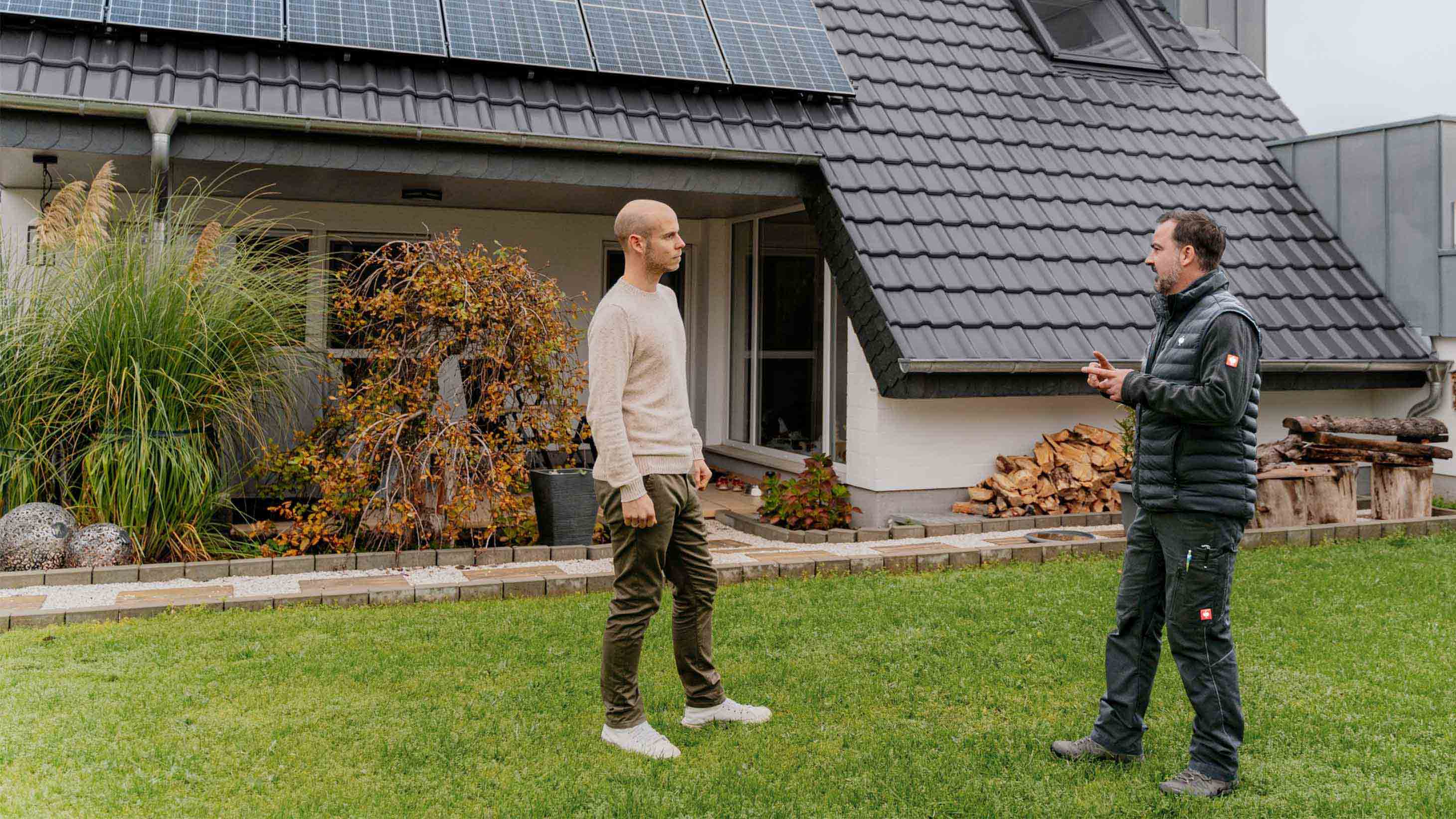 Mann und Fachhandwerker stehen vor einem Altbau mit Photovoltaik