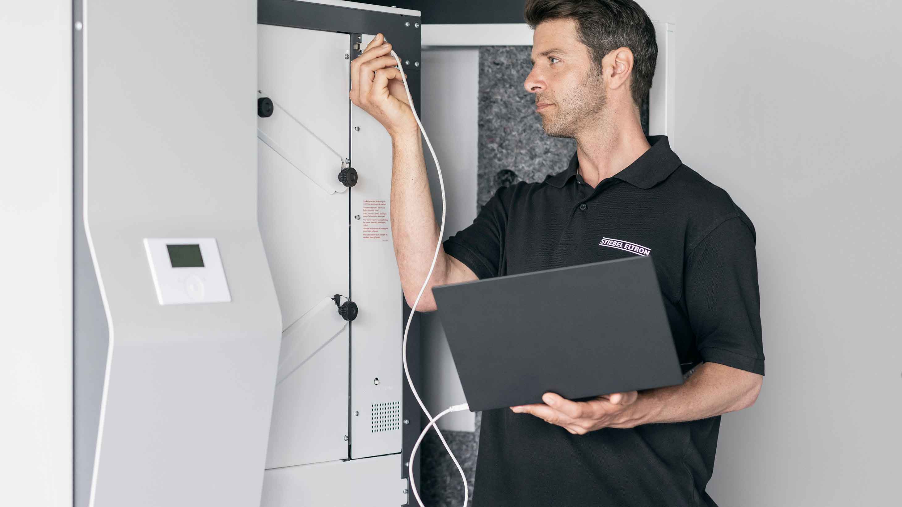 STIEBEL ELTRON-Kundendiensttechniker steht vor einer Wärmepumpe und führt eine Wartung durch